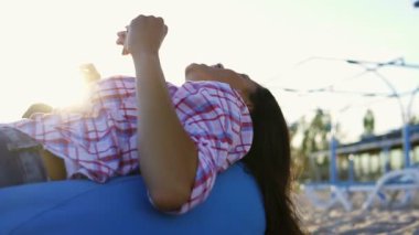 Easychair üzerinde döşeme ve bir adam sahilde oturan ve bir yaz akşamı bir gün batımı sırasında şarkı arkadaş grubu arasında gitar çalmaya dinlerken genç kadın. Slowmotion atış