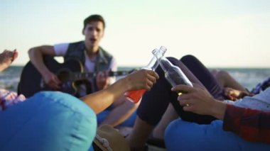 Kokteyller ve bira içme ve sahilde easychairs üzerinde oturan ve bir yaz akşamı bir gün batımı sırasında gitar çalmak bir arkadaş dinlerken alkış yapıyor arkadaş grubu. Slowmotion atış