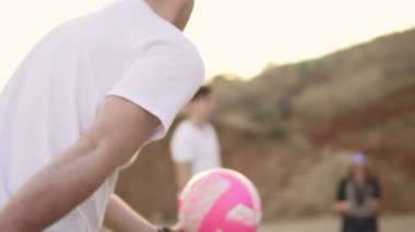Bir topu tekmeleme voleybolcu. Akşam deniz plaj voleybolu top oynarken neşeli genç arkadaşlar. Aktif bir tatil. Slowmotion atış