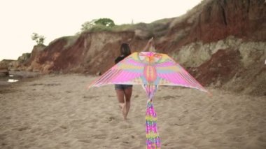 Genç hippi kadını serbest renkli uçurtma sahilde akşamları. Slowmotion atış