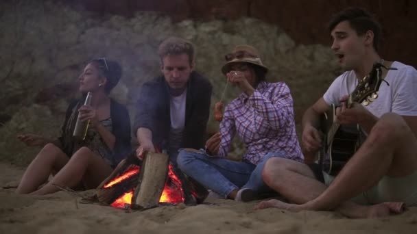 Picnic de jóvenes con hoguera en la playa por la noche. Amigos alegres cantando canciones y tocando la guitarra. Disparo en cámara lenta — Vídeo de stock