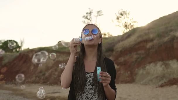 Ung kvinnlig hipster med dreads glatt att göra såpbubblor på stranden på kvällen. Slowmotion skott — Stockvideo