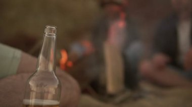 Şömine başında sahilde oturup, bira içme ve marsh mallows ızgara genç arkadaş grubu. Slowmotion atış