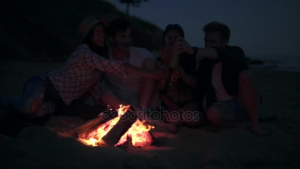 Pique-nique de jeunes avec feu de joie sur la plage le soir en buvant de la bière et en faisant des acclamations. Des amis heureux chantent des chansons et jouent de la guitare. Coup de ralenti — Video