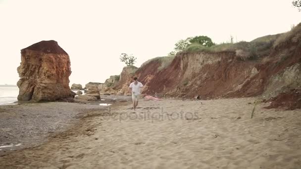 Joven hombre atractivo liberando cometa colorido contra un cielo azul en la playa por la noche. Disparo en cámara lenta — Vídeos de Stock