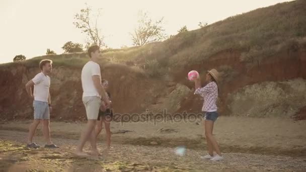 Gioiosi giovani amici che giocano a pallavolo sulla spiaggia in riva al mare durante il tramonto. Teambuilding. Girato in 4k — Video Stock
