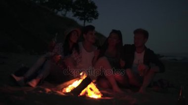 Şarkıları söyleyerek ve birlikte bira içmek sahilde ateş tarafından akşamları oturan genç neşeli arkadaşlar. 4 k'dan fazla vurdu