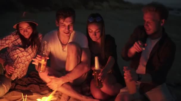 Groep jongeren roosteren met bierflesjes en het hebben van een strand partij op een zomeravond zeggen cheers met bier in 4k — Stockvideo