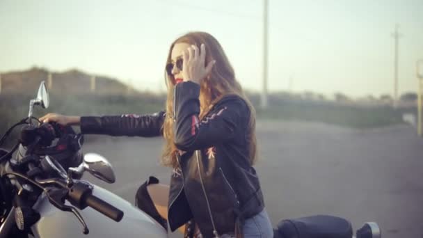 Pretty female biker sitting on the motorcycle seat. Close up of young curly woman in sunglasses on the chopper — Stock Video