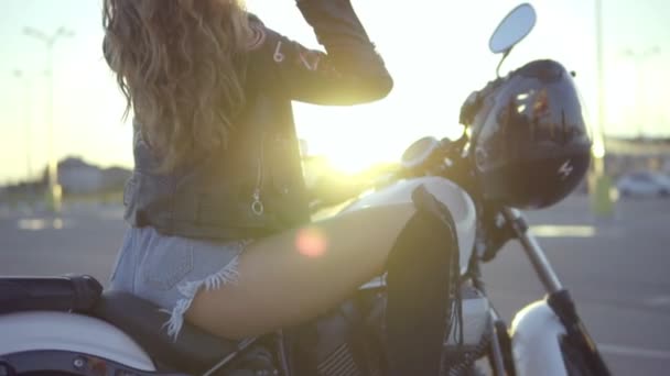 Bella motociclista donna in pantaloncini seduti sul sedile della moto e toccandosi i capelli. Primo piano di giovane donna riccia sexy in occhiali da sole sull'elicottero — Video Stock