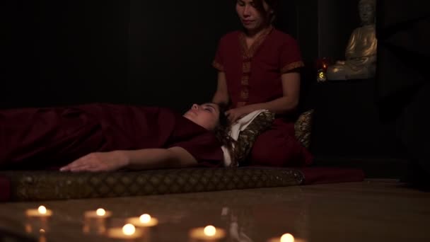 Two thai massage therapists doing thai massage of both head and legs for woman on couch in spa room. Slow motion shot — Stock Video