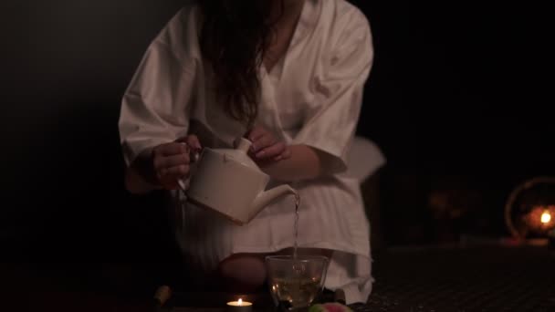 Belle brune en peignoir prenant théière et pooring thé dans une tasse boire tisane au spa au ralenti. Cérémonie du thé thaïlandais. Coup de ralenti — Video