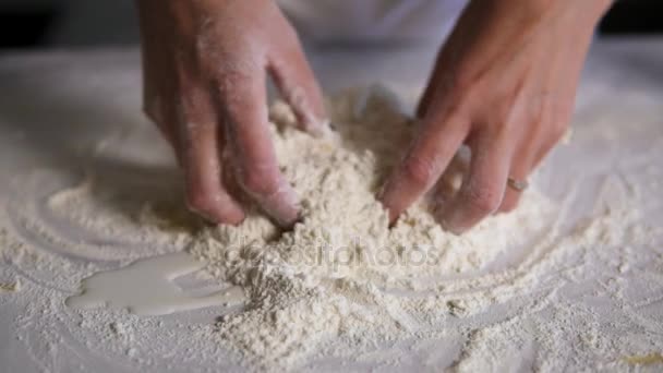 Vista da vicino delle mani femminili che mescolano farina con uova e latte sulla superficie della cucina. Colpo al rallentatore — Video Stock