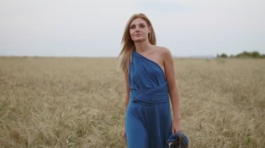 Kameraya bakarak altın buğday alan yürürken uzun mavi elbiseli çekici genç kadın. Özgürlük kavramı. Slowmotion atış