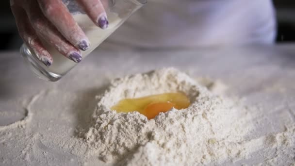 Крупный план женских рук, добавляющих молоко из стекла в муку с яйцами на кухонном столе. Слоумоушн — стоковое видео