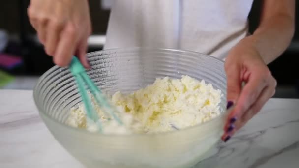 Vista da vicino delle mani femminili che preparano l'impasto mescolando la farina con gli altri ingredienti usando la frusta in cucina. Cibo fatto in casa. Colpo di rallentamento — Video Stock