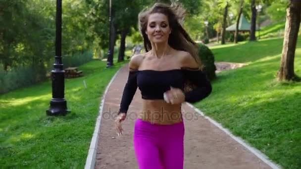 Jovem mulher em sutiã desportivo correndo no parque da cidade ensolarado exercitando ao ar livre. Steadicam estabilizou o tiro, câmara lenta. Exercício matinal. Estilo de vida saudável — Vídeo de Stock