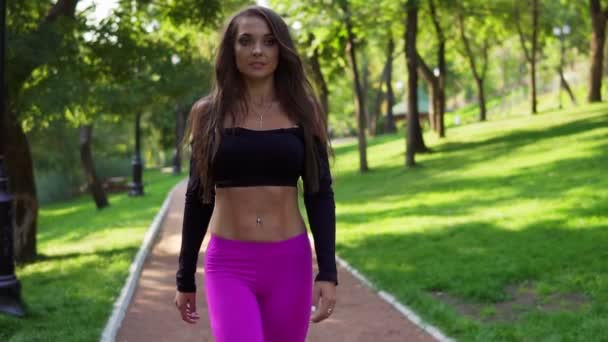 Entrenadora sonriente en top deportivo corto caminando en el parque después de un entrenamiento intensivo. Ajuste sano deporte mujer haciendo ejercicio en la mañana. Disparo en cámara lenta — Vídeo de stock