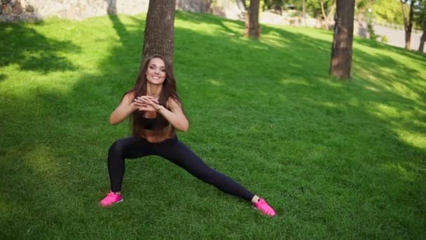 Flexibles junges Mädchen, das sich nach einer langen herausfordernden Laufeinheit im grünen Stadtpark bei schönem sonnigen Morgen auf dem Rasen im Park ausstreckt — Stockvideo