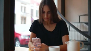 Uzun saçlı ve doğal makyaj cep telefonu kafede kullanarak genç bayan yoğunlaşmıştır. Modern cihazlarla kullanım. Online alışveriş