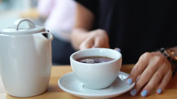 Vista de cerca de las manos femeninas tomando una taza blanca con té caliente de la mesa de madera. Entonces la cámara se mueve hacia arriba con una taza y esta mujer comienza a beber su té. Disparo en cámara lenta — Vídeo de stock