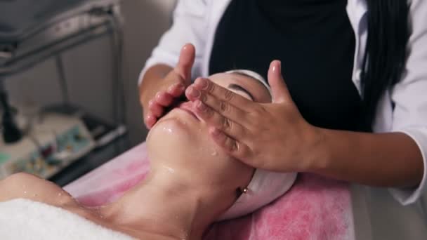 Yüz ve boyun spa salonda masaj yapma bir profesyonel kozmetik eller closeup görünümü. Genç kadın kozmetik yüz işlem sırasında kanepede yatıyor. Güzellik, sağlıklı ve genç kavramı — Stok video