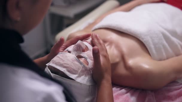 Closeup view of a professional cosmetologists hands making face massage to the young woman with mask on her face and neck during cosmetic face procedure. Face care — Stock Video