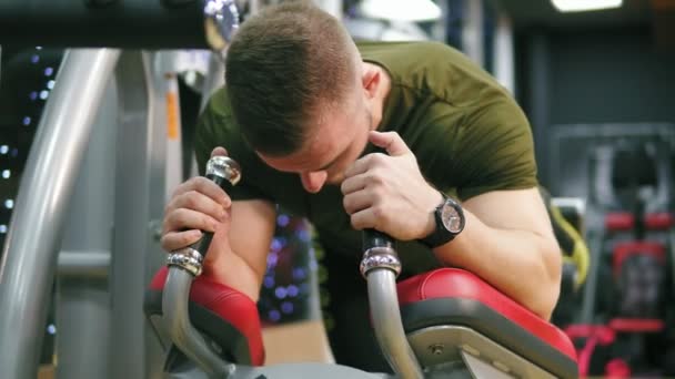 Der junge, athletische Mann stemmt Gewichte an den Beinen auf Fitnessgeräten im Fitnessstudio und blickt nach vorn. Schuss in 4k — Stockvideo