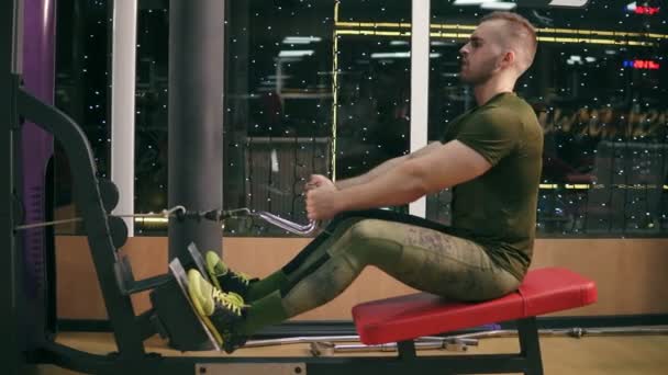 Disparo en 4k: vista lateral de un hombre en el gimnasio haciendo tira hacia atrás con peso. El hombre atractivo está entrenando los músculos de la espalda usando la máquina de cable de ejercicio para la masa corporal. Ejercicio y culturismo concepto deportivo — Vídeo de stock