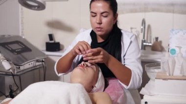 Profesyonel güzellik uzmanı pamuk sünger kullanarak kadının yüzü temizliyor. Genç kadın kozmetik yüz yordamı spa salonda sırasında kanepede yatıyor. Yüz bakımı. Güzellik, sağlıklı ve genç kavramı