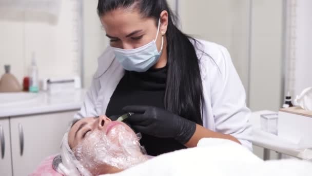 Выстрел в 4k: профессиональный комсетолог в маске делает несколько инъекций в щеке женщины во время мезотерапии. Биоревитализация и подтяжка лица, нехирургическое лечение — стоковое видео