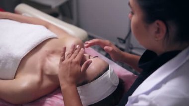 Kanepede yatan ve o yüz kremi uyguluyor süre onun profesyonel güzellik uzmanı konuşuyor ve spa salonda masaj surat closeup görünümü bir kadının gözleri ile kapalı