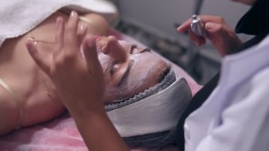 Portre profesyonel güzellik uzmanı apllying özel muamele kadının yüzünde ise kanepede yatan genç kadın bir bakış. Profesyonel Cilt Bakımı spa salonda genç kadın