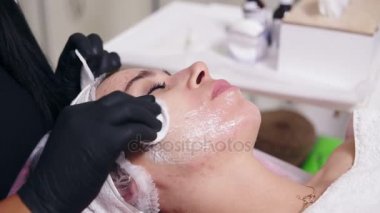 Pamuk sünger kullanarak kadının yüz temizliğinde profesyonel güzellik uzmanı closeup görünümü. Genç kadın kozmetik yüz yordamı spa salonda sırasında kanepede yatıyor. Yüz Bakımı