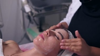 Genç kadın Spa salonda peeling profesyonel almak. Şevval Özçelik Güzellik bir genç kız yüz, yüz masaj yapıyor temizlik cilt yüz peeling uygulama çalışan el,