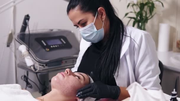 Professionele schoonheidsspecialist is toepassing van gezichtscrème en gezicht massage voor jonge vrouw verdienen met Smet huid liggend op de Bank in spa salon — Stockvideo