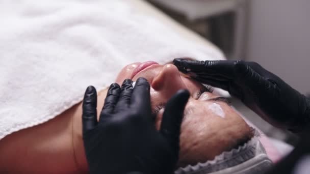 Närbild bild av en kvinna med fläck huden liggande på soffan medan professionell kosmetolog tillämpar ansiktskräm och gör ansiktet massage i spasalong — Stockvideo