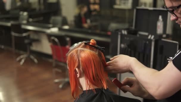 Una joven vistiéndose el pelo en peluquería. Estilista-peluquero en el trabajo. Hombre peluquero cepillado pelo en salón de belleza. Disparo en cámara lenta — Vídeos de Stock