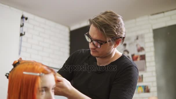 Stylischer männlicher Friseur mit Brille schneidet rothaarige Frauenhaare im Schönheitssalon. junge Frau, die sich die Haare schneiden lässt und sich im Friseursalon kleidet. Schuss in Zeitlupe — Stockvideo