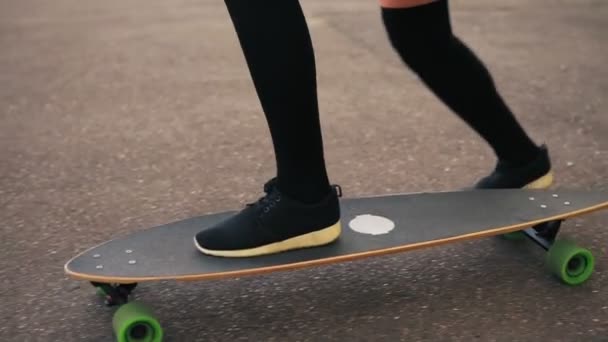 Wyświetlić zbliżenie womans nogi w czarne trampki skateboarding na drodze w mieście. Nogi na deskorolce. Slowmotion strzał — Wideo stockowe