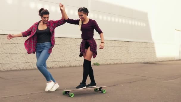 笑っている若い流行に敏感な女の子を教えている彼女の手を握って支えている友人によってスケート ボードします。スローモーション撮影 — ストック動画