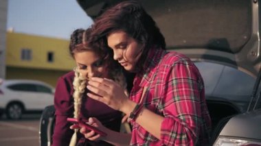 Park açık araba bagajında içinde otururken resimler güneşli gün boyunca alışveriş merkezi tarafından kontrol smartphone vasıl arıyorsunuz iki genç çekici kız closeup görünümü