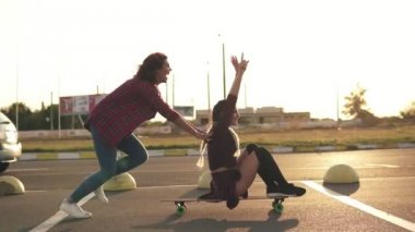 Yan görünümü bir kadının elleri onun arkadaşı arkasında bastırıyor iken bir longboard üzerinde oturan ve gün batımı sırasında çalışan kaldırdı. Hayattan zevk. Mercek parlaması. Slowmotion atış