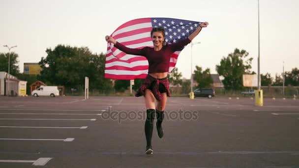 Jovem menina americana feliz correndo enquanto segurando a bandeira americana e olhando para a câmera. Tiro em câmara lenta — Vídeo de Stock