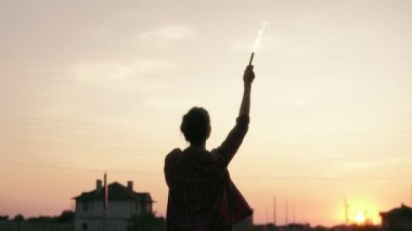 Genç kadın havai fişek mumlar ile günbatımı sırasında ayakta ve kamera arıyorum. Mercek parlaması. Slowmotion atış