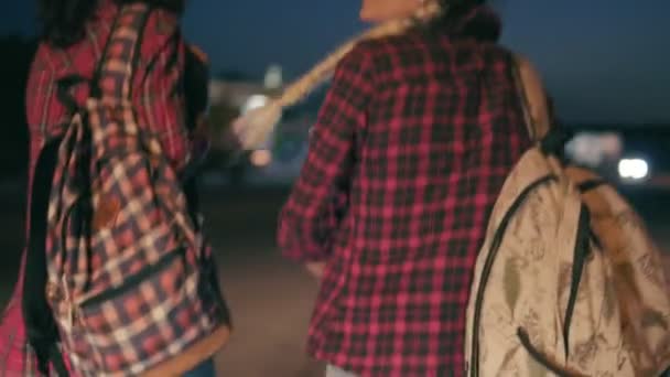 Deux jeunes femmes auto-stoppeuses se tiennent sur la touche tenant leurs sacs à dos et demandent d'arrêter les voitures qui passent la nuit en été — Video