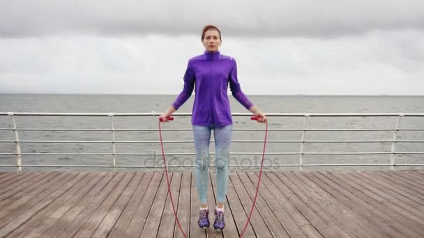 Young woman working out on the jump rope. Outdoor sports. Girl jumping on a skipping rope by the sea. Slowmotion shot — Stock Video