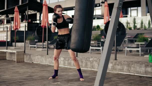 Female boxer exercising outdoors. Beautiful athletic woman in gloves punching a bag outside. Self defence concept. Slowmotion shot — Stock Video