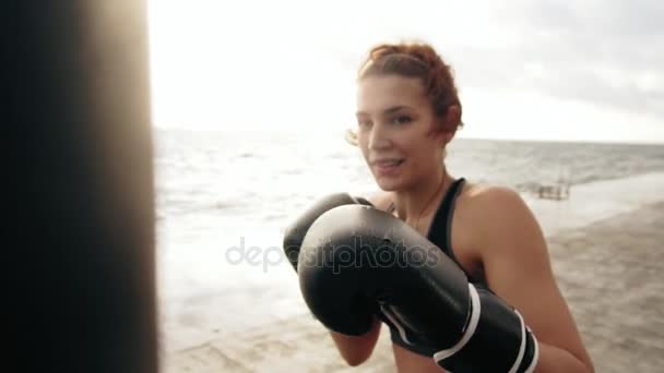 海で太陽に対してバッグ運動手袋の強い運動女性ボクサーのクローズ アップ ビュー。女性ボクサーのトレーニングします。自己防衛の概念。スローモーション撮影 — ストック動画