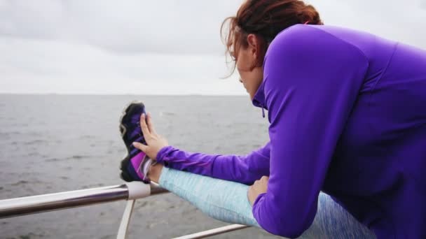 早朝の海のビーチでジョギングする前に彼女の足を伸ばし若い女性の背面図をクローズ アップ。夏のビーチでトレーニング — ストック動画